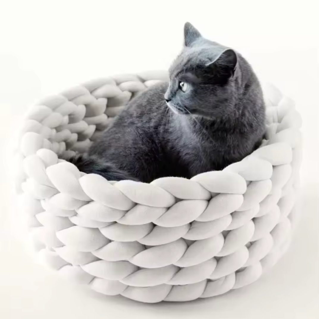 Handgewebtes Katzenbett Grey cat resting in a handmade blue chunky knit cat bed on a light carpet – modern and cozy pet furniture design. Graue Katze liegt entspannt in einem handgewebten, blauen Katzenbett aus dickem Chunky-Strick auf einem hellen Teppich – modernes und gemütliches Design für Haustiere.